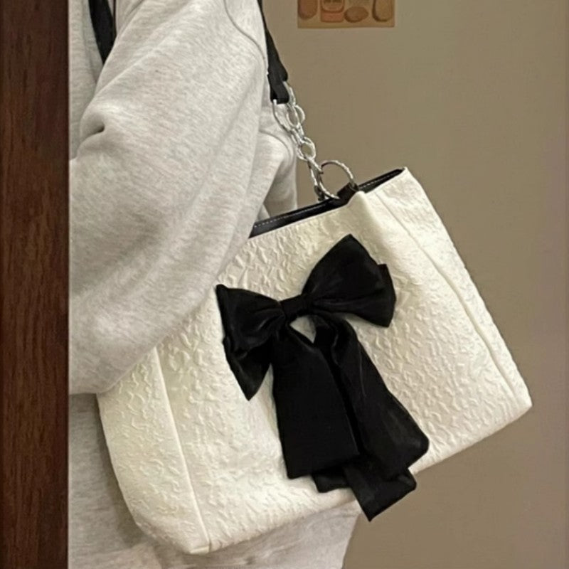 White textured handbag with a black bow held by a person wearing a white coat.